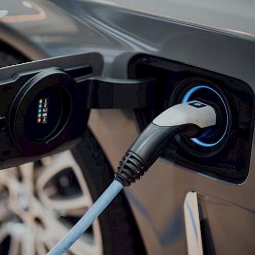 An electric vehicle is being charged, with a charging plug connected to the charging port on the car.