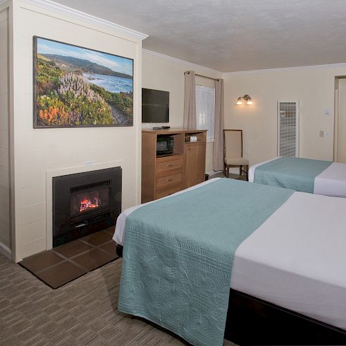 The image shows a hotel room with two beds, a fireplace, a desk, a chair, a TV, a dresser, and a scenic painting above the fireplace.