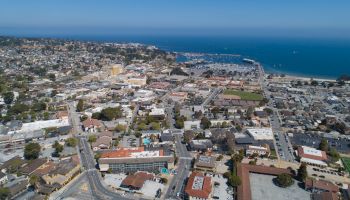 This image depicts an aerial view of a coastal city with numerous buildings, roads, and a marina by the ocean, extending into the distance.