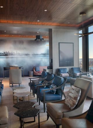 A modern lounge area with comfortable seating, large windows offering a sea view, and a wall mural depicting a city skyline ending the sentence.