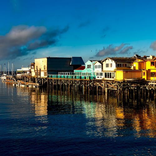 Colorful buildings on a pier by a calm body of water, with numerous boats docked in the background under a clear blue sky.