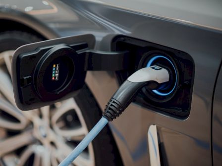 The image shows an electric car being charged with a charging plug connected to the vehicle's charging port.